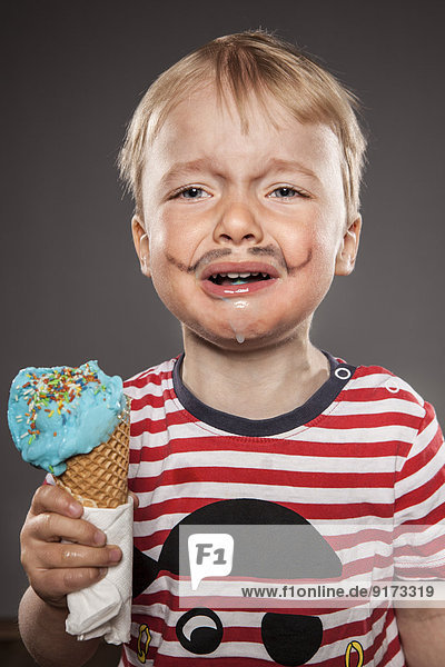 Portrait of crying looking little boy with painted beard and ice cream