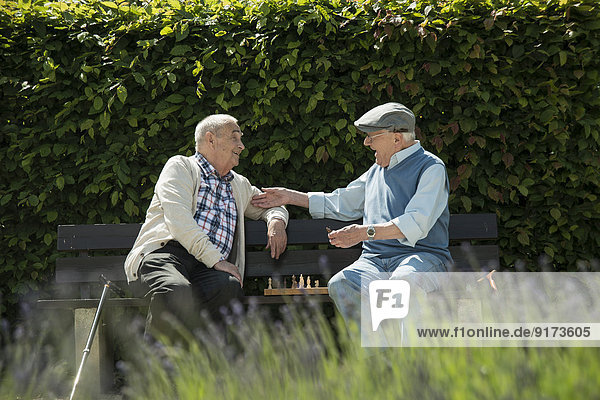 Two old friends sitting on park bench playing chess