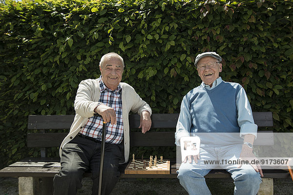 Two old friends sitting on park bench with chess