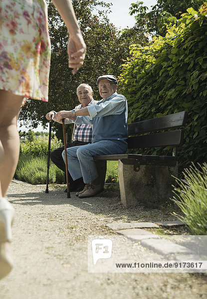 Zwei alte Männer sitzen auf der Parkbank und beobachten die Beine der vorbeifahrenden Frau.