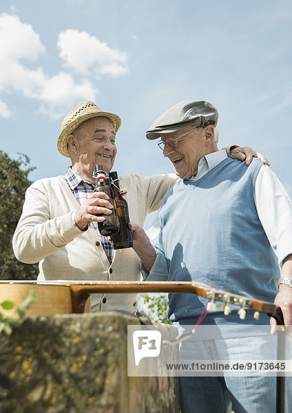 Zwei alte Freunde stoßen mit Bierflaschen im Park an.