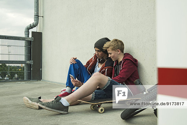 Two boys sitting on ground looking at cell phone