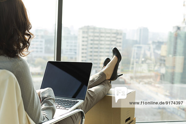Businesswoman using laptop with feet on cardboard boxes