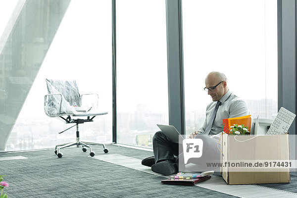 Businessman using laptop on empty office floor with cardboard box