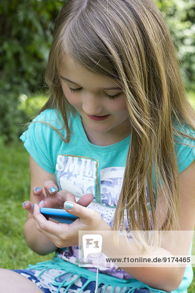 Kleines Mädchen sitzend mit Smartphone im Garten