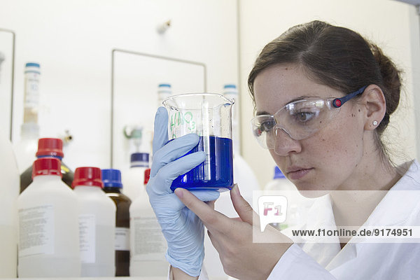 Portrait einer jungen Chemikerin mit Becher mit blauer Flüssigkeit