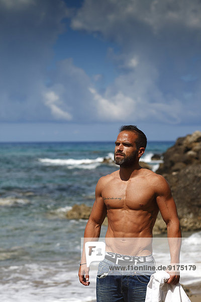 Griechenland  Ionische Inseln  Korfu  Mann ohne Hemd  der das Sonnenlicht vor dem Meer genießt