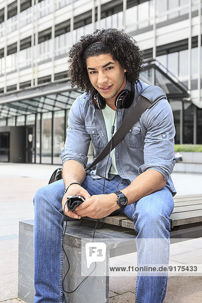 Junger Student auf der Bank sitzend mit seinem Smartphone