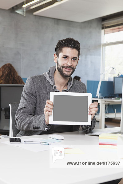 Portrait of smiling man showing tablet computer in the office