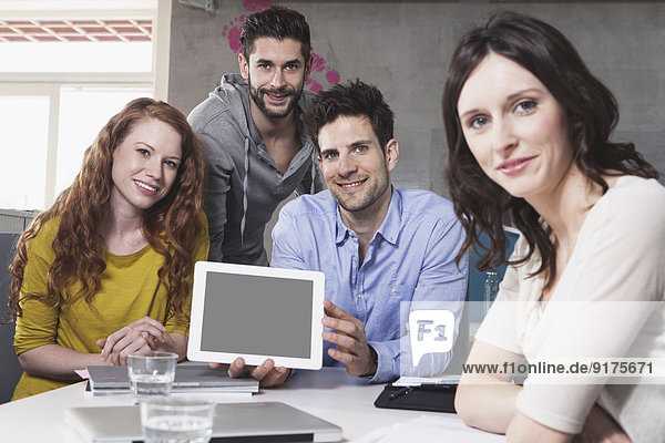 Gruppenbild von vier kreativen Menschen  die einen Tablet-Computer im Büro zeigen.