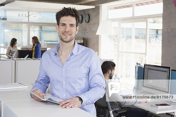 Porträt eines lächelnden Mannes mit Tablet-Computer im Büro