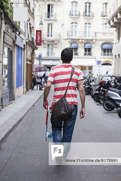 Frankreich  Paris  Mann mit Skateboard  der auf einer Straße läuft.