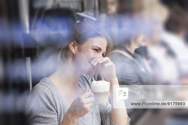Frankreich  Paris  Porträt einer lachenden jungen Frau  die in einem Café Milchkaffee trinkt.