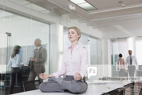 Deutschland  München  Geschäftsfrau im Büro  Meditation auf dem Schreibtisch