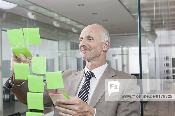 Germany  Munich  Businessman in office  putting sticky notes on glass pane