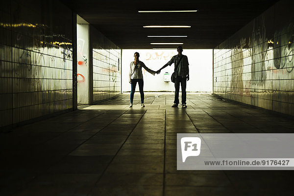 Young couple standing hand in hand in a dark underpass