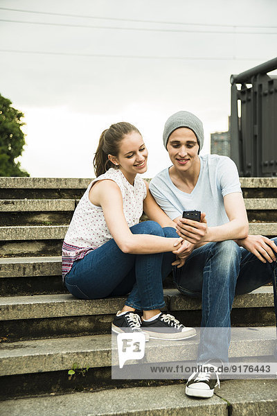 Young couple with smartphone sitting on stairs