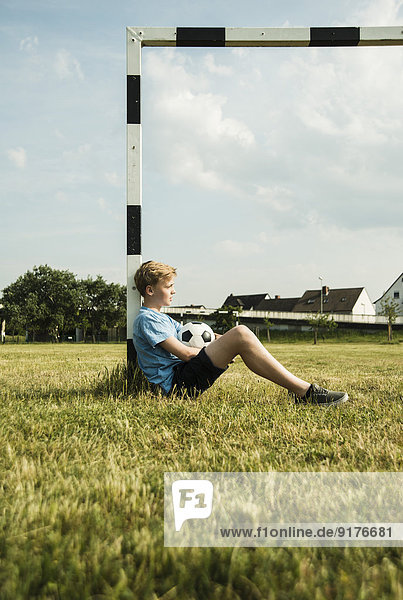 Deutschland  Mannheim  Teenager auf Rasen sitzend  am Tor lehnend