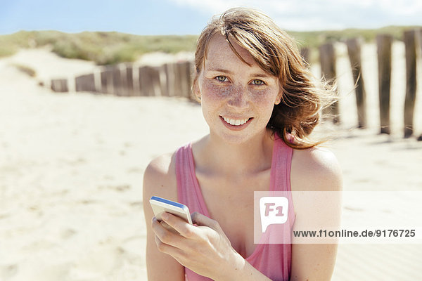 Porträt einer Frau mit Smartphone am Strand