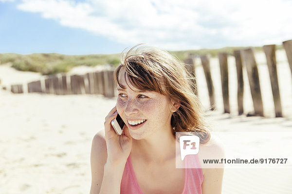 Porträt einer Frau beim Telefonieren mit ihrem Smartphone am Strand