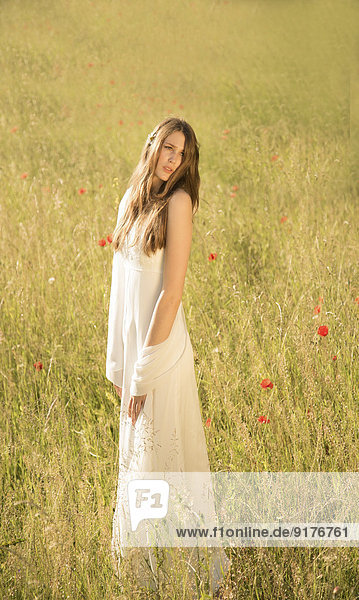 Porträt eines jungen Mädchens in weißem Kleid auf der Wiese stehend