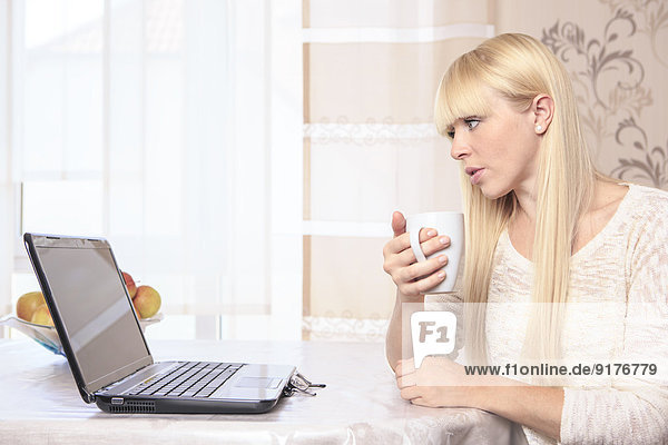 Portrait of a young woman with a cup using laptop at home