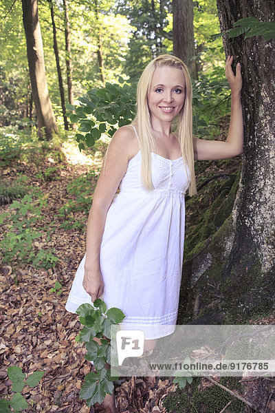 Porträt einer jungen Frau  die sich auf einen Baumstamm im Wald stützt.
