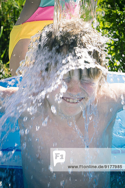 Mädchen spritzt Wasser auf Bruder im aufblasbaren Pool