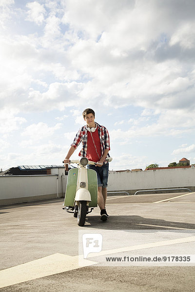 Teenage boy with motor scooter on parking lot