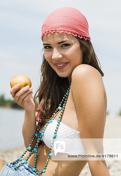 Porträt einer jungen Frau mit Apfel am Strand