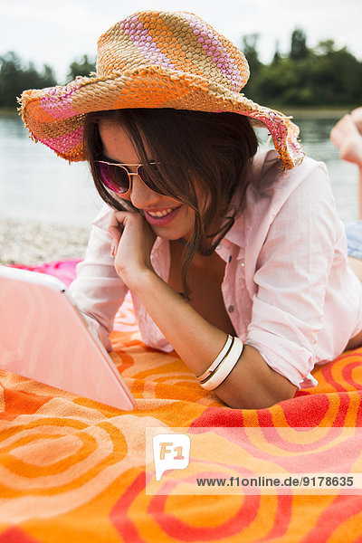 Porträt einer lächelnden jungen Frau mit Sommerhut und Sonnenbrille mit digitalem Tablett