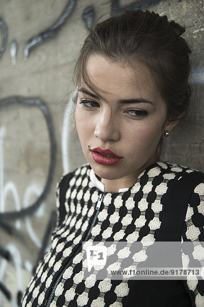 Portrait of sad young woman with red lips in front of wall with graffiti