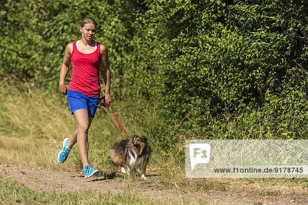 Junge Frau beim Joggen mit Hund auf dem Feldweg