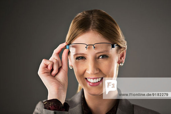 Portrait of confident businesswoman raising eyeglasses