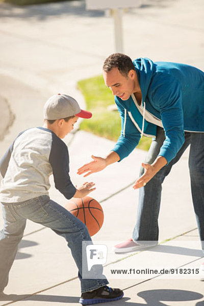 Vater und Sohn spielen Basketball in sonniger Einfahrt