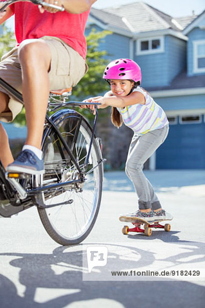 Daughter on skateboard pushing father on bicycle