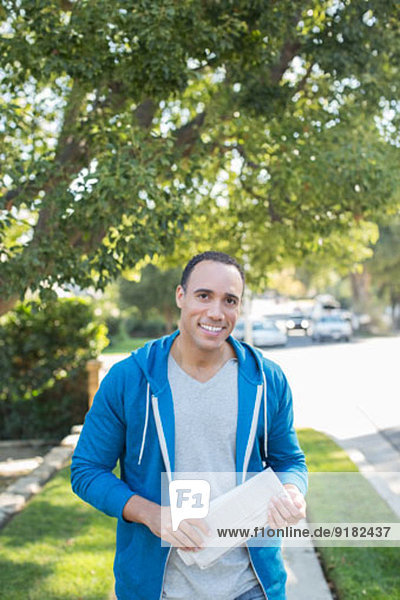 Portrait of smiling man with newspaper on sidewalk