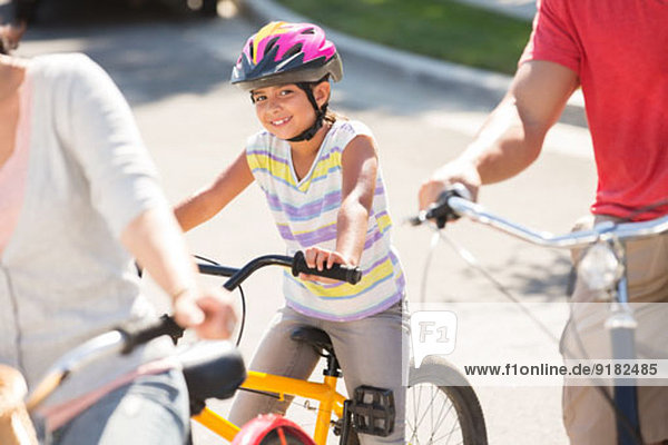 Porträt eines lächelnden Mädchens auf dem Fahrrad mit Eltern