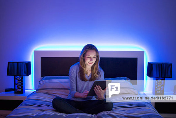 Frau mit digitalem Tablett auf dem Bett