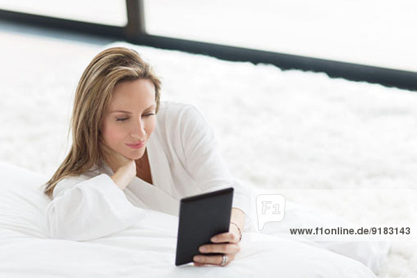 Frau im Bademantel mit digitalem Tablett im Schlafzimmer