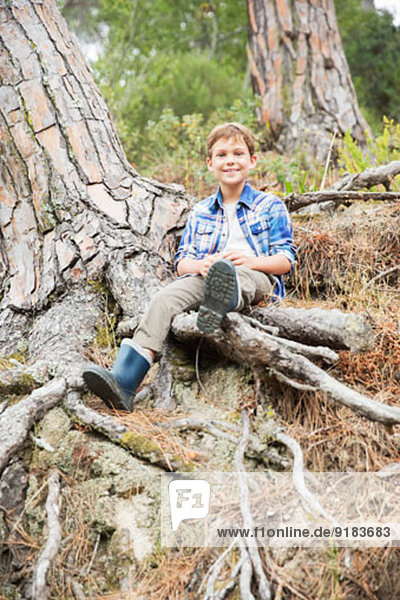 Junge auf Baumwurzeln im Wald sitzend