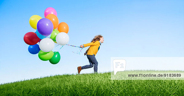 Mädchen spielt mit Ballons auf grasbewachsenem Hügel