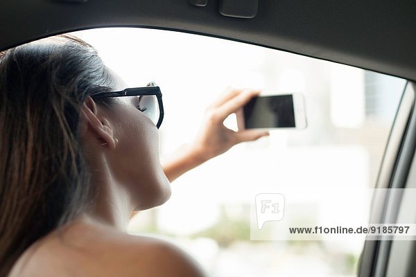 Young woman photographing with smartphone from taxi window
