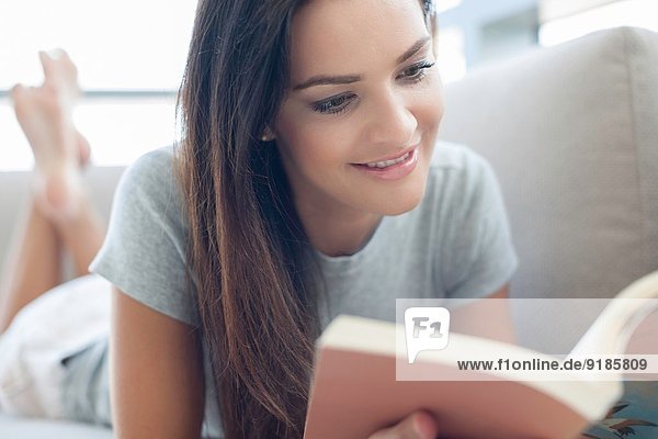 Close up of young woman on sofa reading book