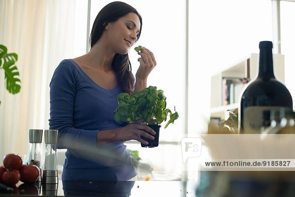 Young woman smelling basil plant in kitchen