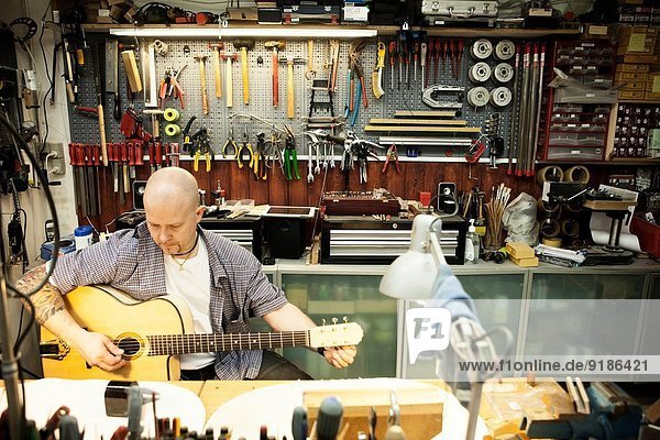 Gitarrenbauer beim Stimmen der Akustikgitarre in der Werkstatt