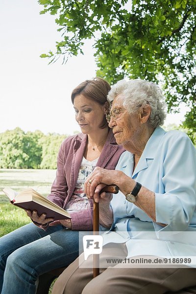 Seniorin und Enkelin sitzen auf der Parkbank und lesen die Bibel.