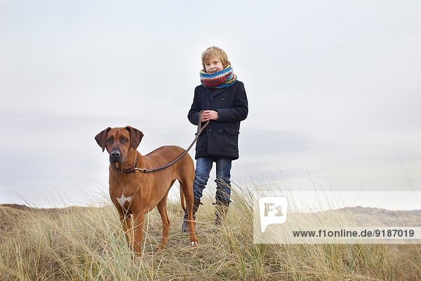 Junge geht mit seinem Hund in Sanddünen an der Küste spazieren