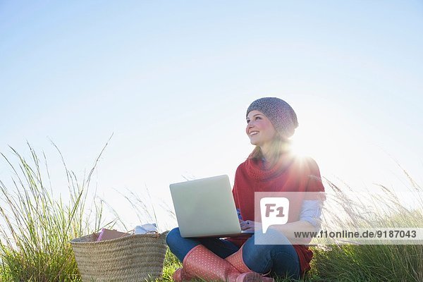 Junge Frau im langen Gras sitzend mit Laptop
