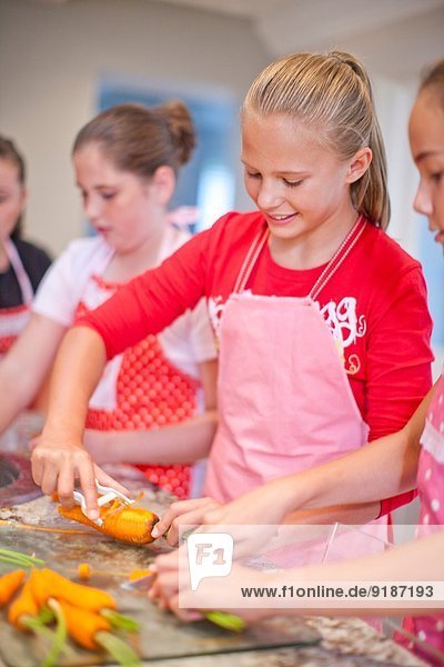 Teenage girls preparing carrots in kitchen
